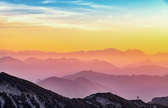 Colorful sunrise over misty mountains in Altmünster, Austria with a lone hiker silhouette.
